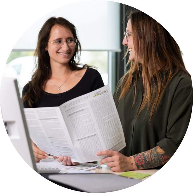 Zwei Mitarbeiterinnen stehen an einem Schreibtisch und betrachten gemeinsam ein Dokument.